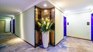 Un pasillo de hotel con una planta central, un muro curvo y suelo alfombrado.