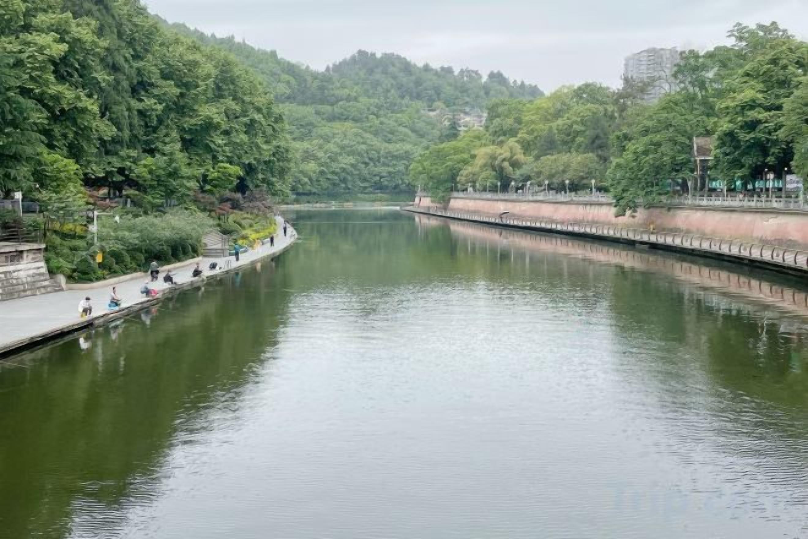 A calm river with a walkway on one side and a bridge on the other.