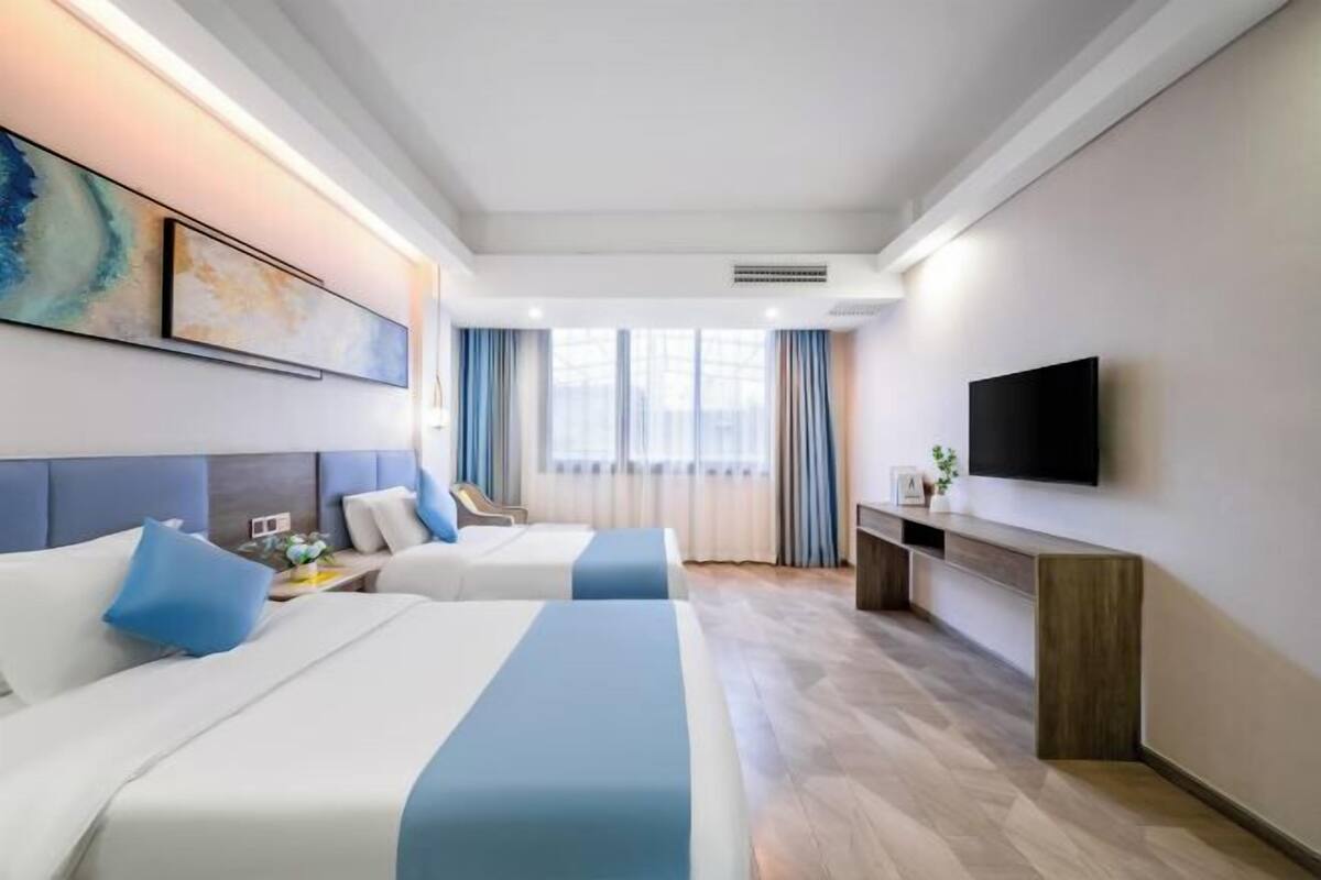 A hotel room with two beds, a TV, a desk, and a window with curtains.