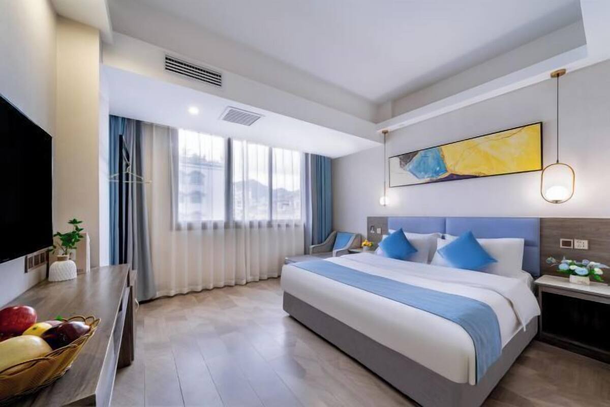 A modern hotel room with a large bed, a flat-screen TV, a fruit basket, and a city view.