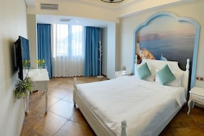 A hotel room with a large bed, a TV, a desk with a vase of flowers, and a view of a coastal landscape through the window. - Biyun Lanting Hotel (Zunyi Huizhi) (Zunyi)
