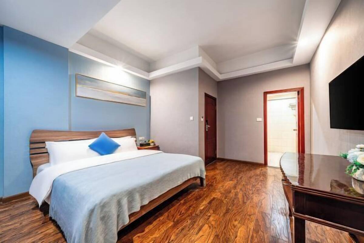 A hotel room with a bed, a wooden floor, a TV, and a door leading to another room.