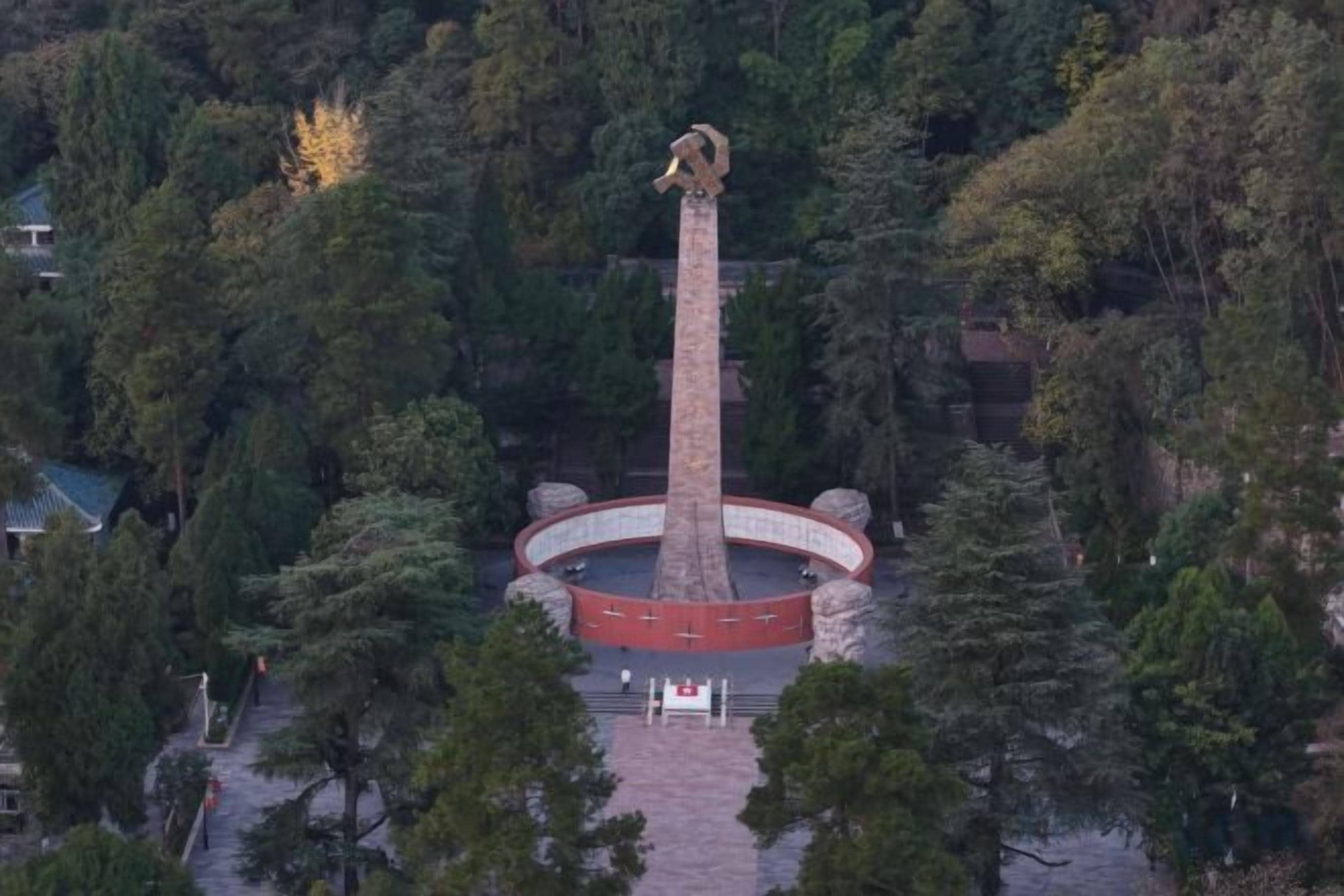 Um monumento rodeado por árvores e uma praça circular.