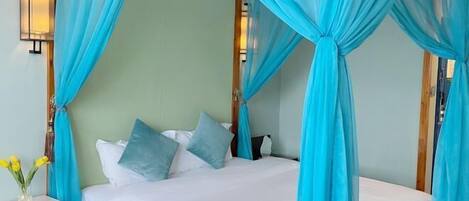 A bed with a canopy, a bedside table with a vase of flowers, and wall-mounted lights.