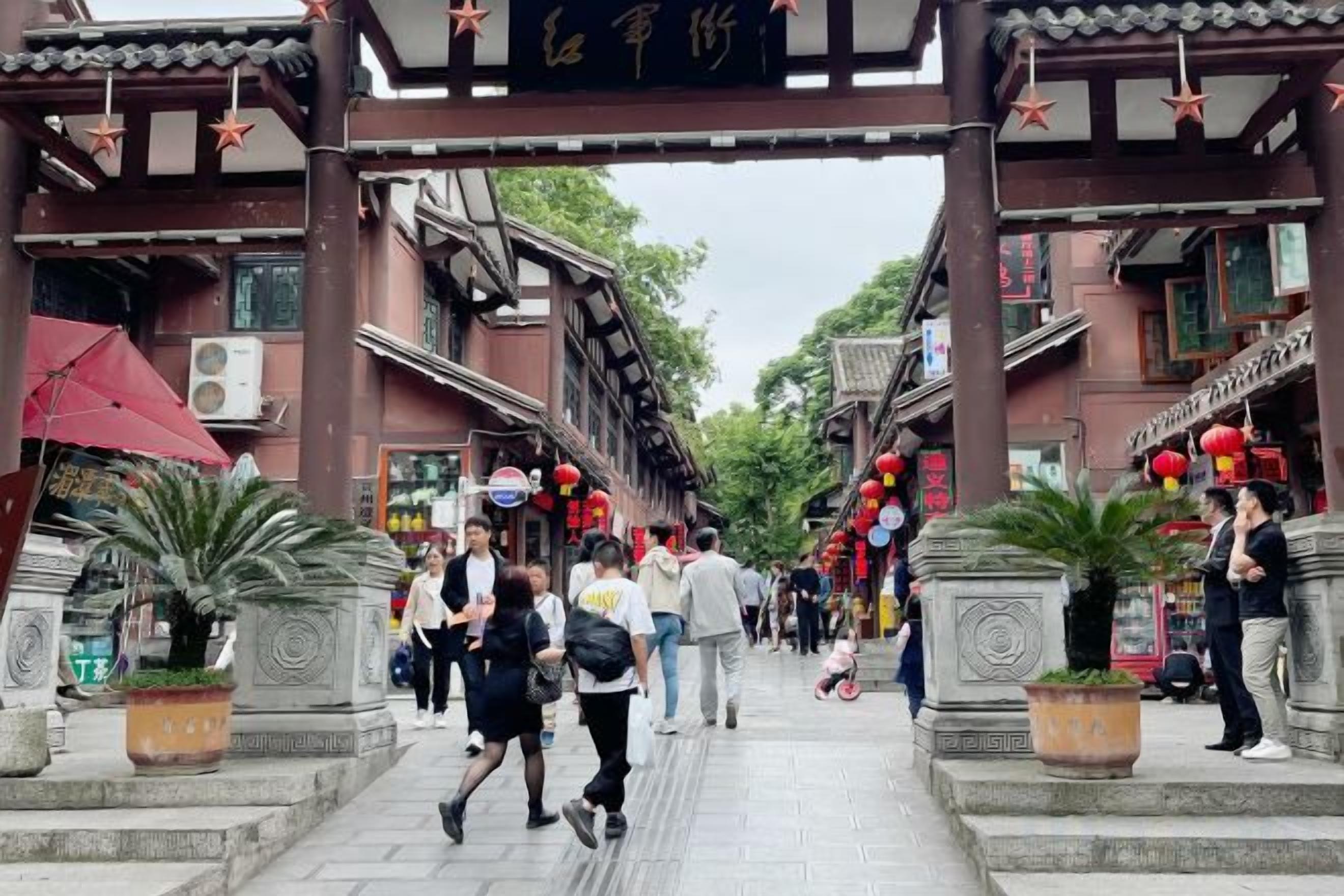 A traditional street with a covered entrance, potted plants, and people walking.
