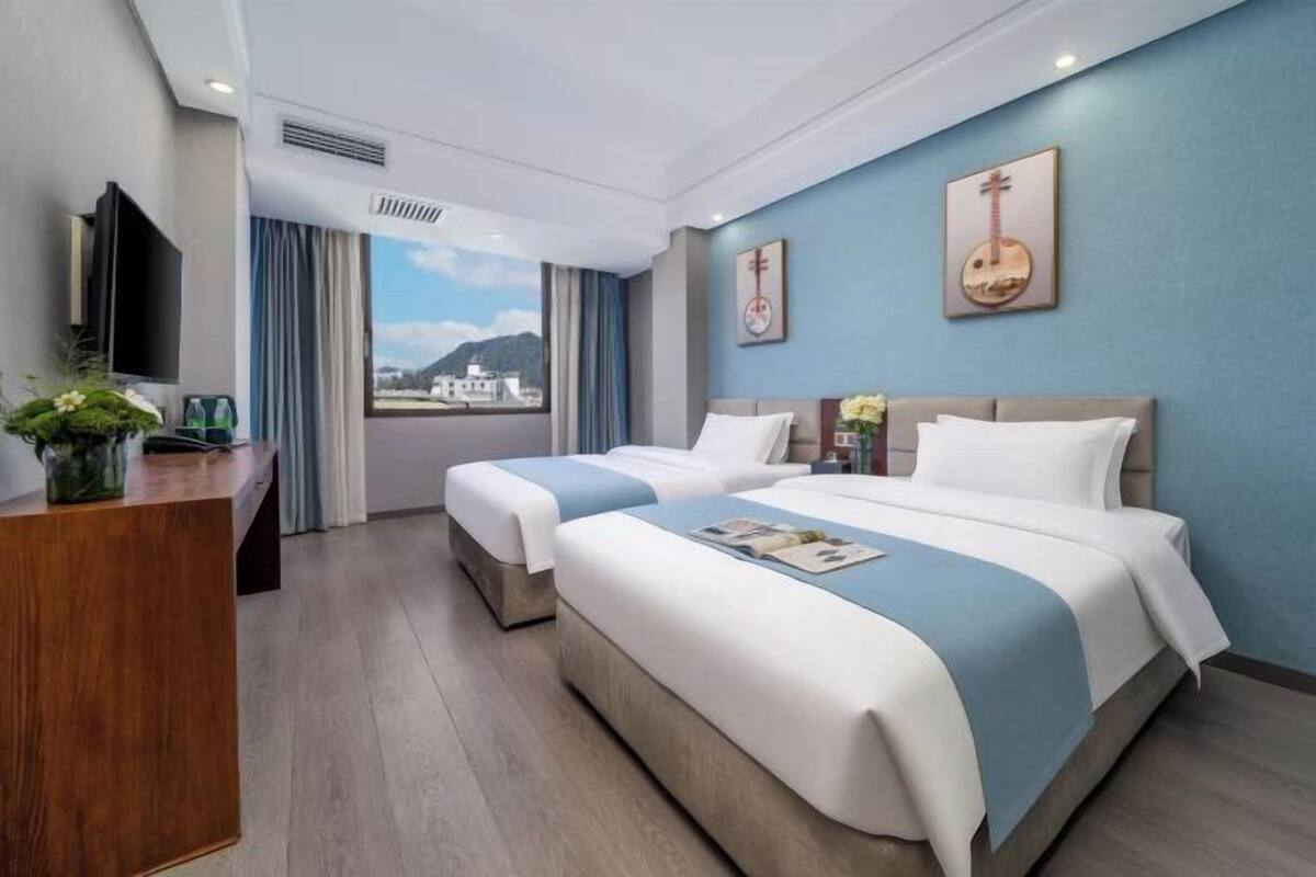 A hotel room with two beds, a desk, a TV, and a view of the mountains.
