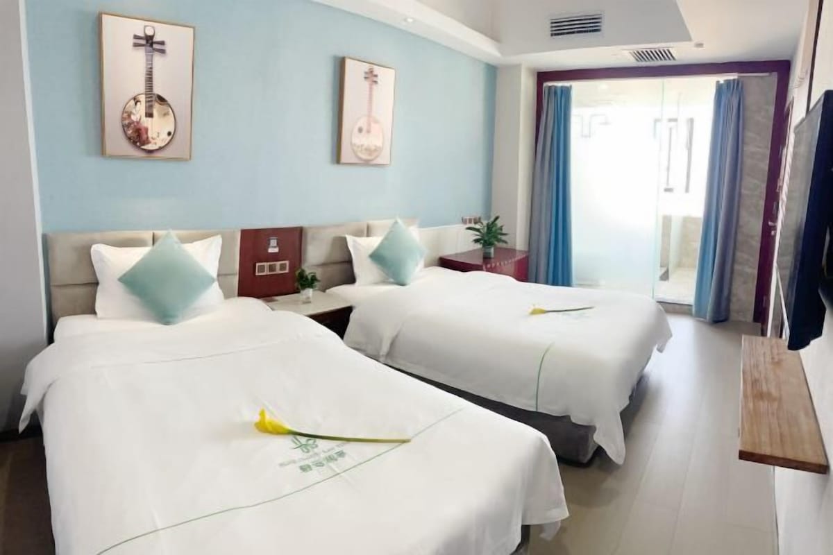 A hotel room with two beds, a small table, a mirror, and a window with curtains.