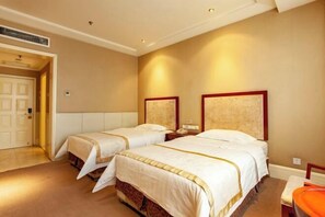 Une chambre d’hôtel avec deux lits, une table de chevet avec une lampe, une chaise et une porte donnant sur une autre pièce.