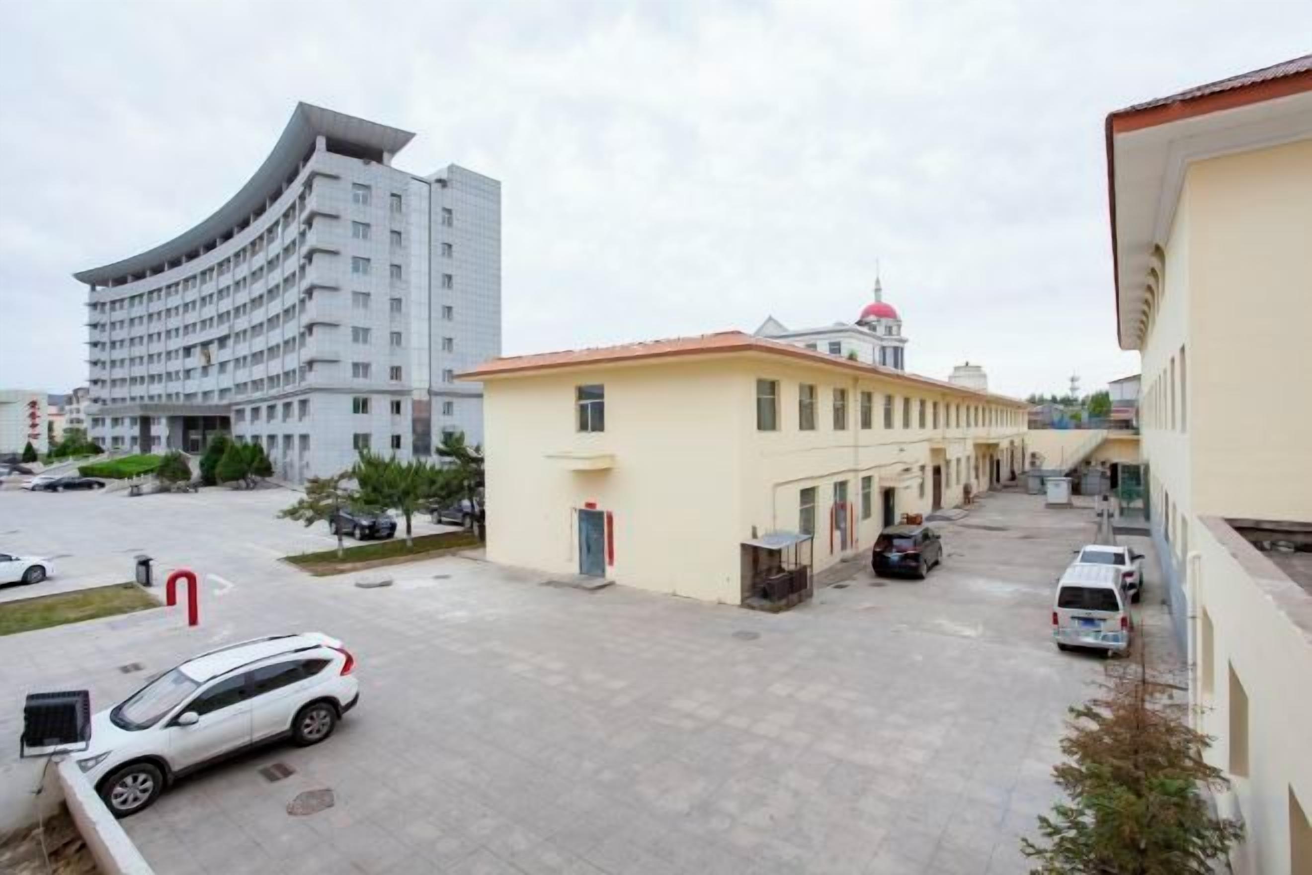 Un espace de stationnement avec un bâtiment en arrière-plan, un bâtiment jaune avec un toit rouge, et une voiture blanche garée au premier plan.