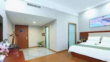 A hotel room with a wooden floor, a bed with white bedding, a desk with a coffee maker, and a painting on the wall.