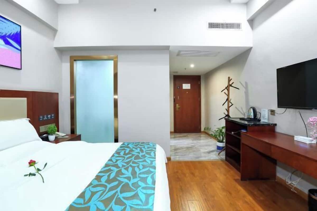 A hotel room with a bed, a desk, a television, and a door leading to another room.