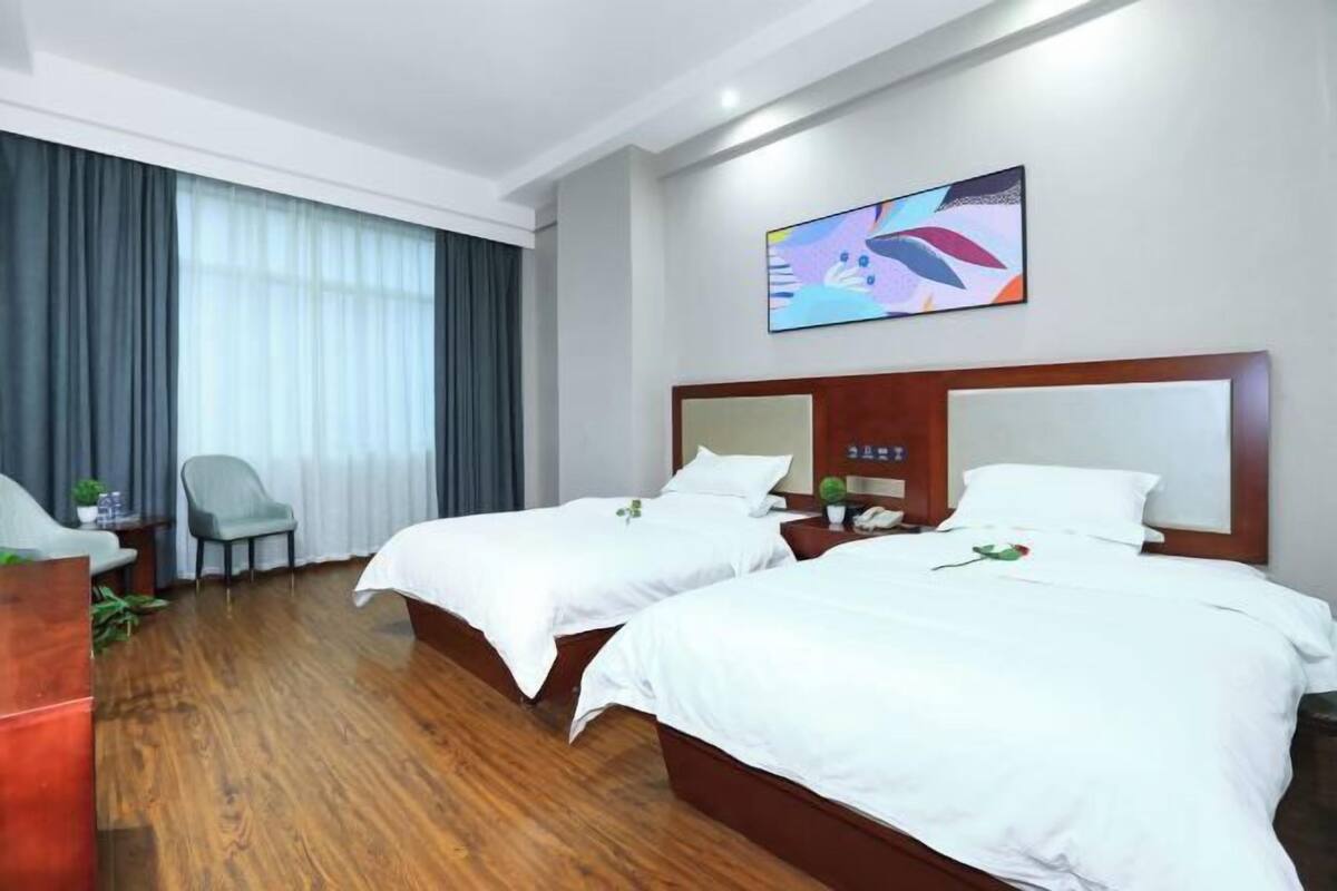 A hotel room with two beds, a TV, a desk, and a chair.