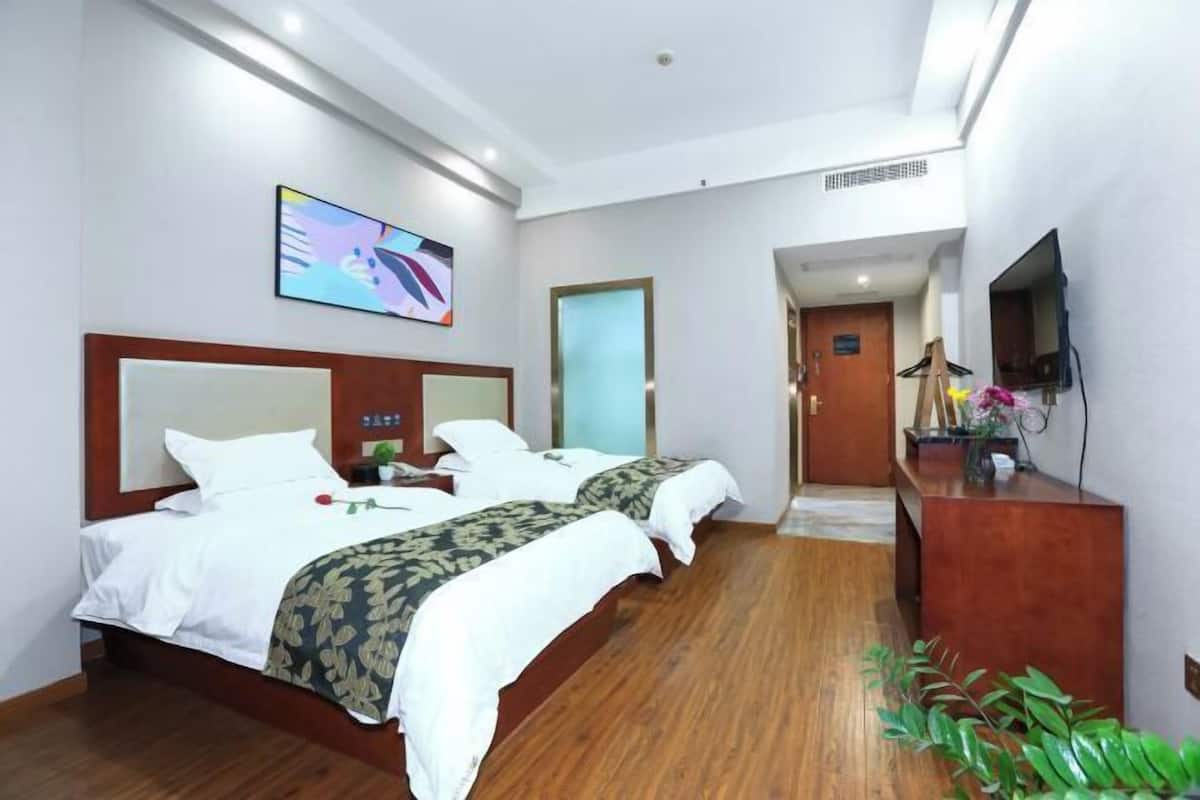 A hotel room with two beds, a desk, a TV, and a painting on the wall.