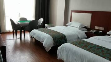 A hotel room with two beds, a desk with chairs, a lamp, and a window with curtains.