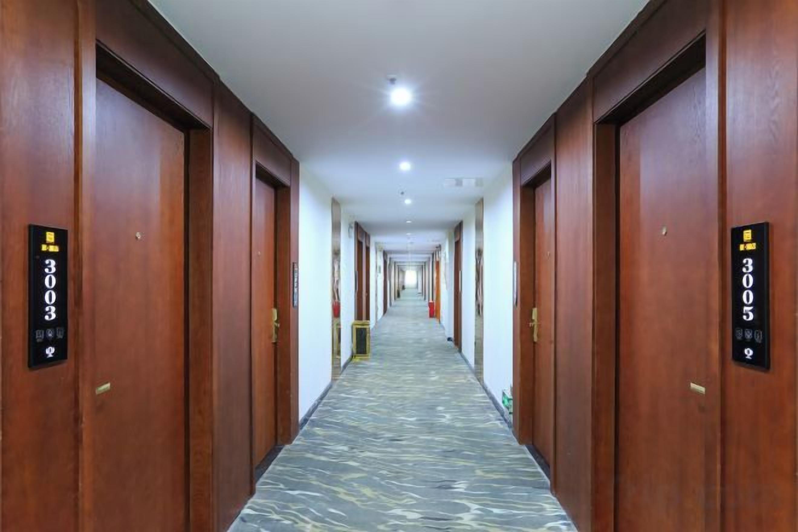 Un pasillo de hotel con puertas de madera, letreros con números de habitación y un suelo con diseño de mármol.