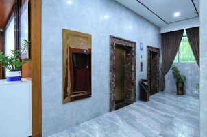 Vestíbulo de hotel con suelo de mármol, detalles de madera y plantas en macetas.