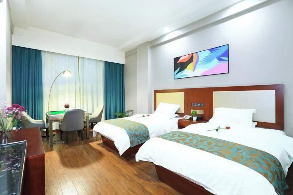 A hotel room with two beds, a desk, a chair, and a large window with curtains.