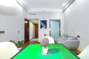 A modern hotel room with a green pool table, a round table with a decorative centerpiece, a grey sofa, and a small potted plant.