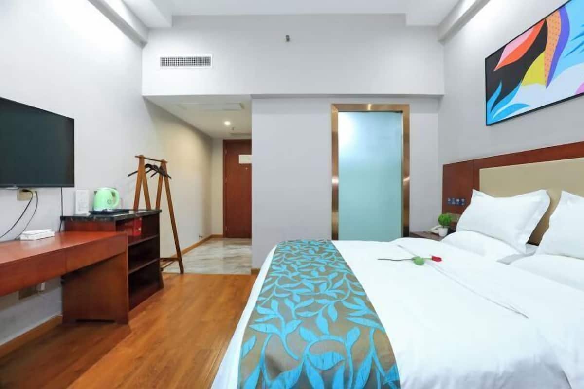 A hotel room with a bed, a desk, a television, and a painting on the wall.