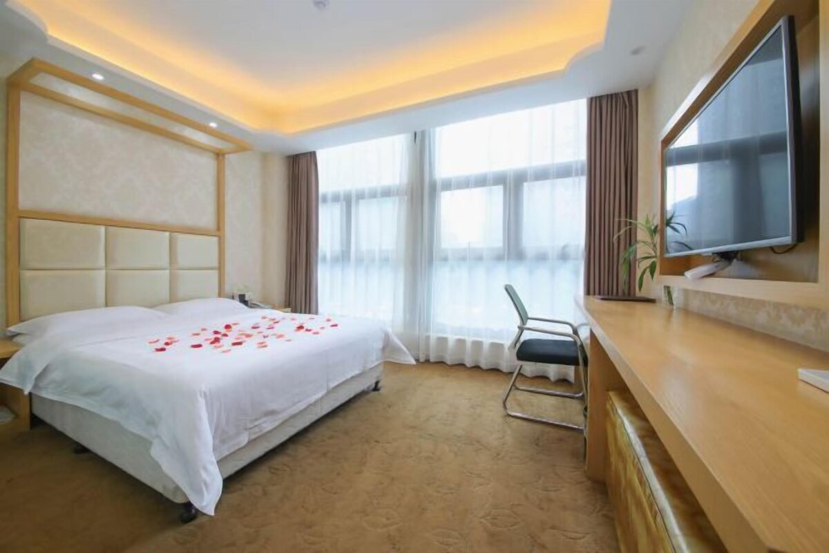 A hotel room with a large bed, a desk, a television, and a window with curtains.