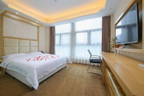 A hotel room with a large bed, a desk, a television, and a window with curtains.