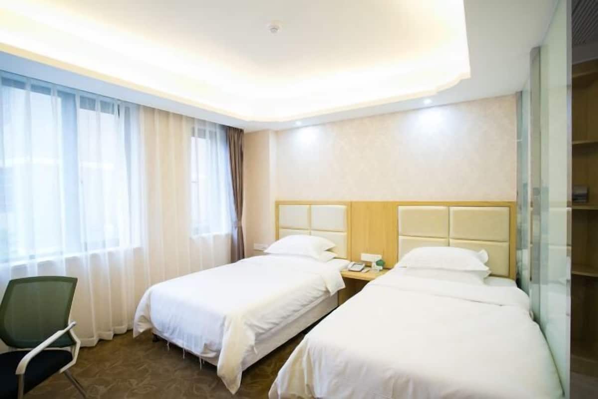 Habitación de hotel con dos camas, una silla y una mesita de noche con un teléfono y una botella.