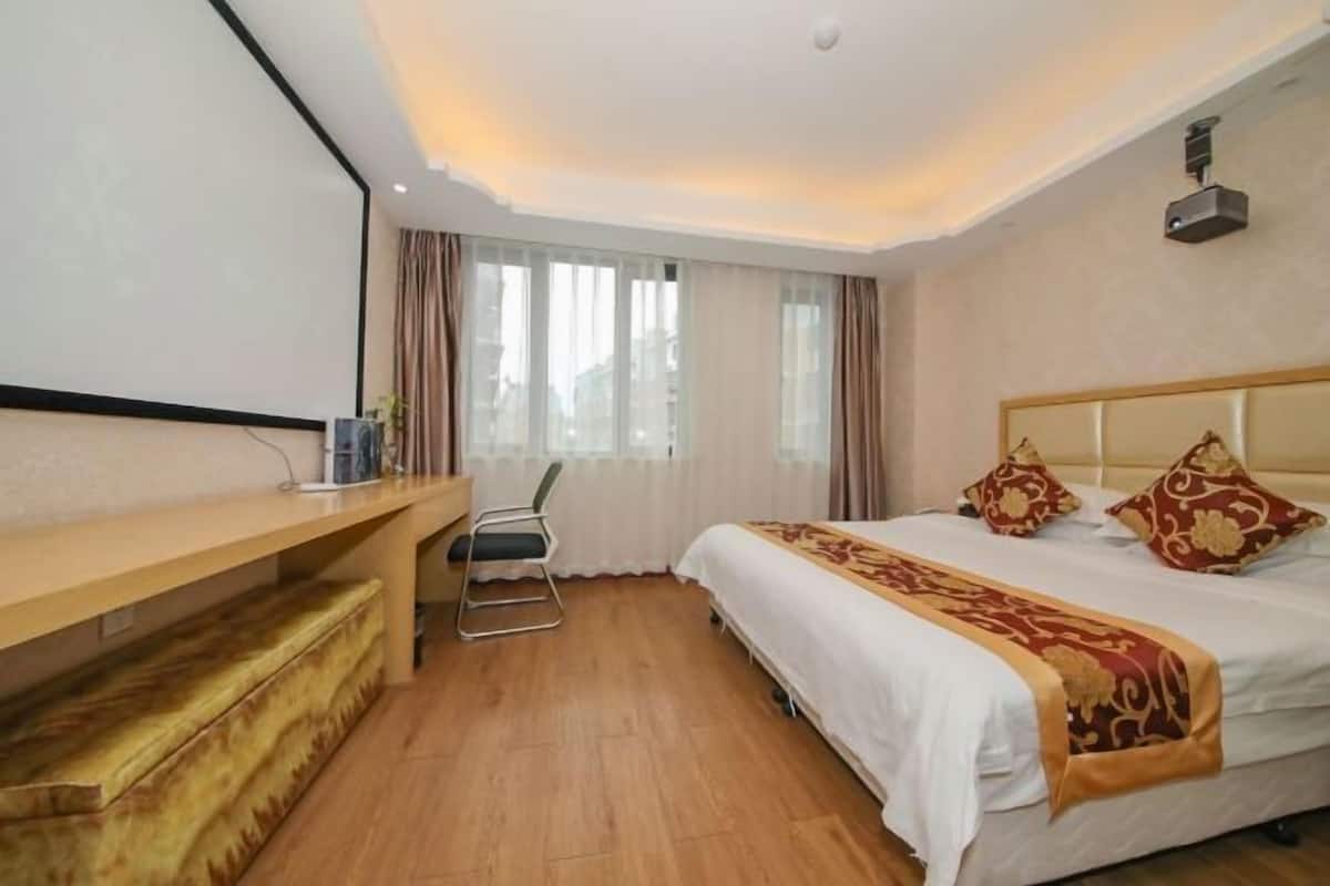 Una habitación de hotel con cama, escritorio, silla y ventana con cortinas.
