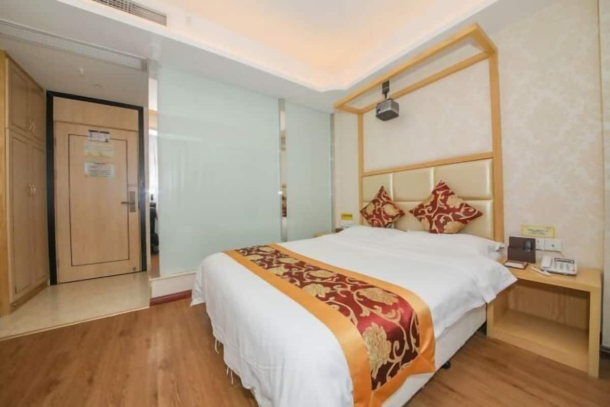 Habitación de hotel con cama, mesita de noche y una puerta a la izquierda.