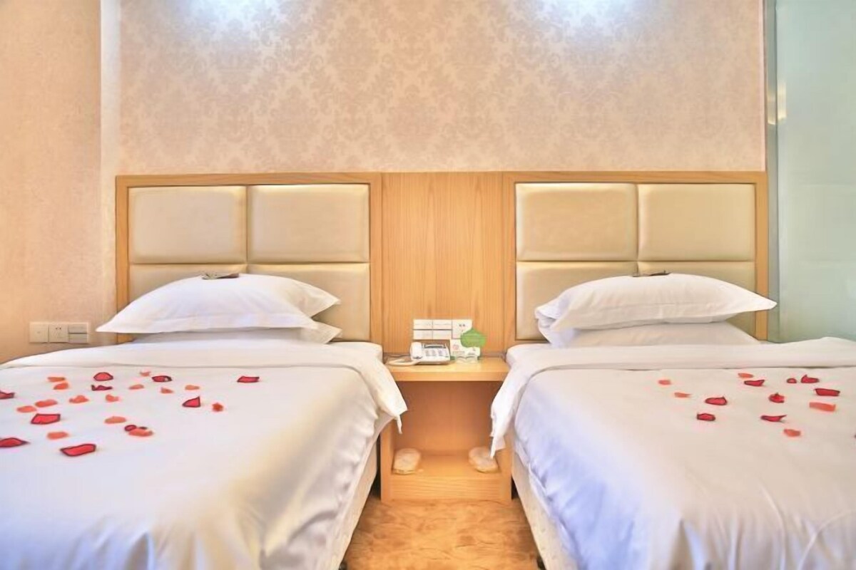 A hotel room with two beds, a wooden headboard, a bedside table with a phone, and rose petals on the beds.