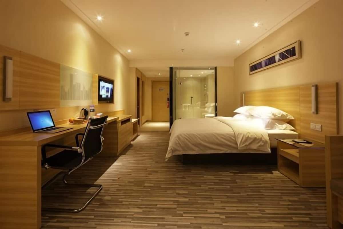 A hotel room with a bed, desk, chair, TV, and a small bathroom.