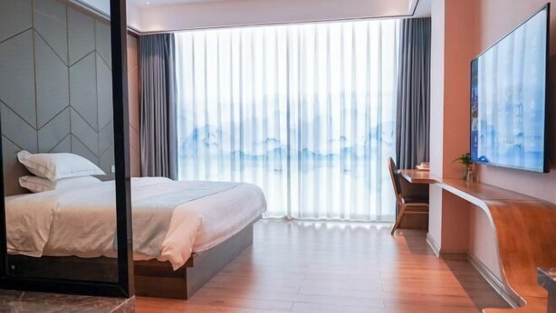 A modern hotel room with a large bed, a desk, and a TV mounted on the wall. - Shibazi Hotel (Yangjiang)