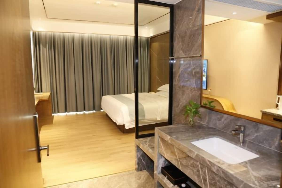 A modern hotel room with a large bed, a marble bathroom sink, and a large mirror.