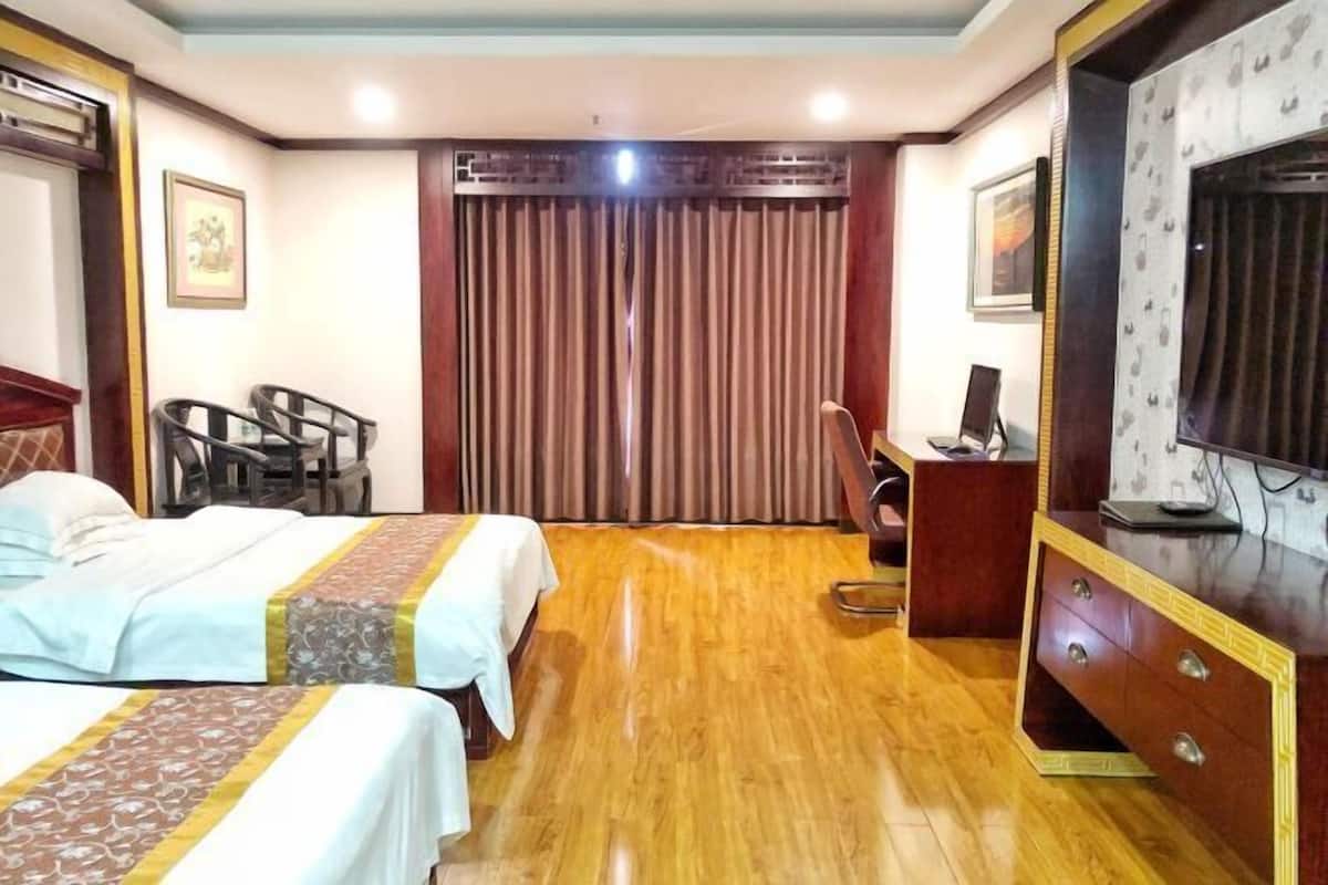 A hotel room with two beds, a wooden floor, a desk with a chair, a television, and a curtain.