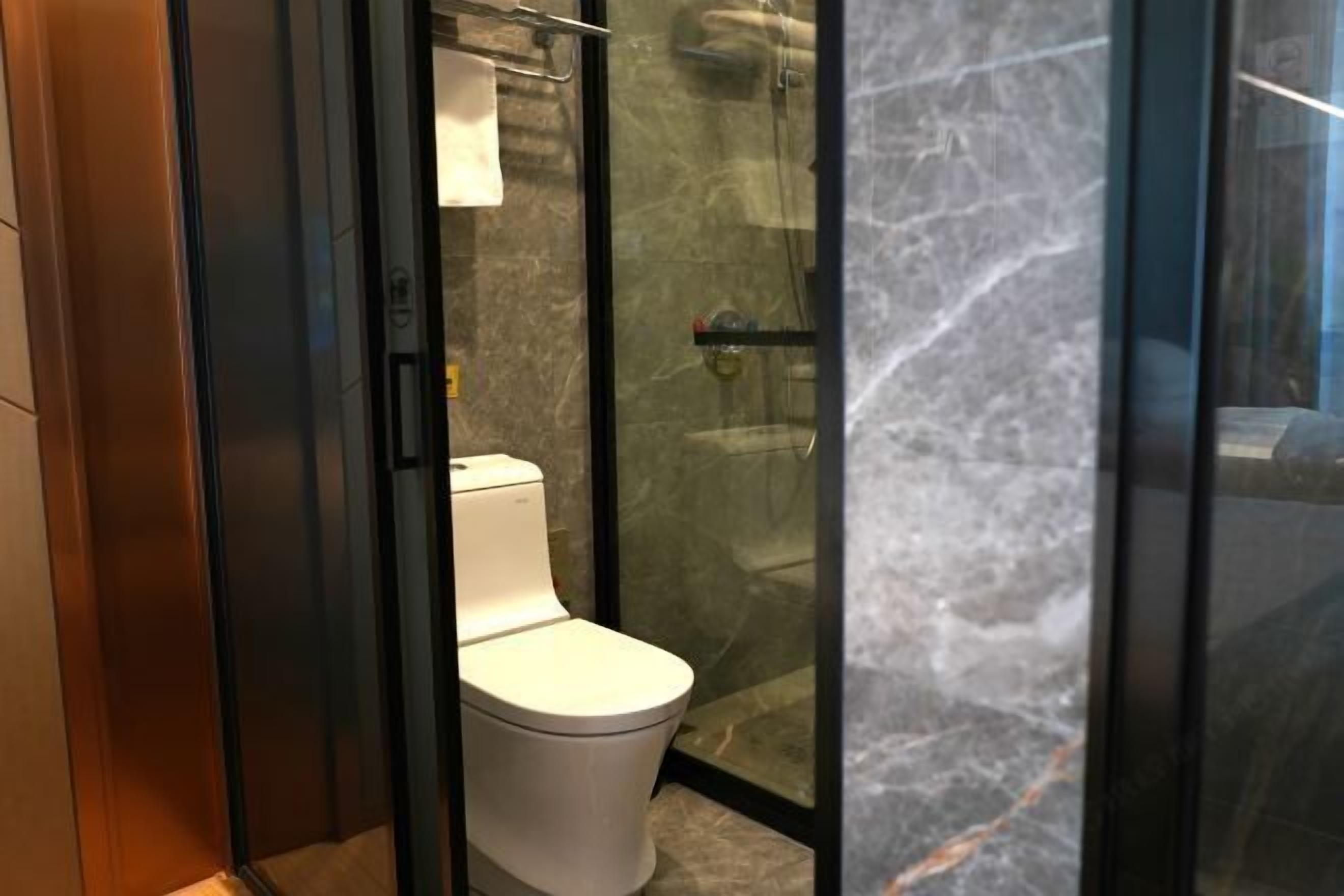 A modern bathroom with a glass-enclosed shower, a toilet, and a marble floor.