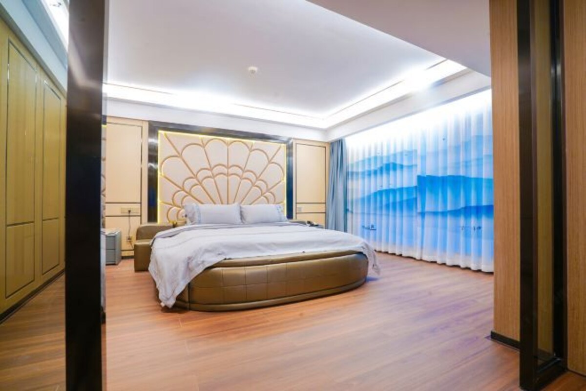 A modern bedroom with a curved bed, a decorative headboard, and a large window with curtains.