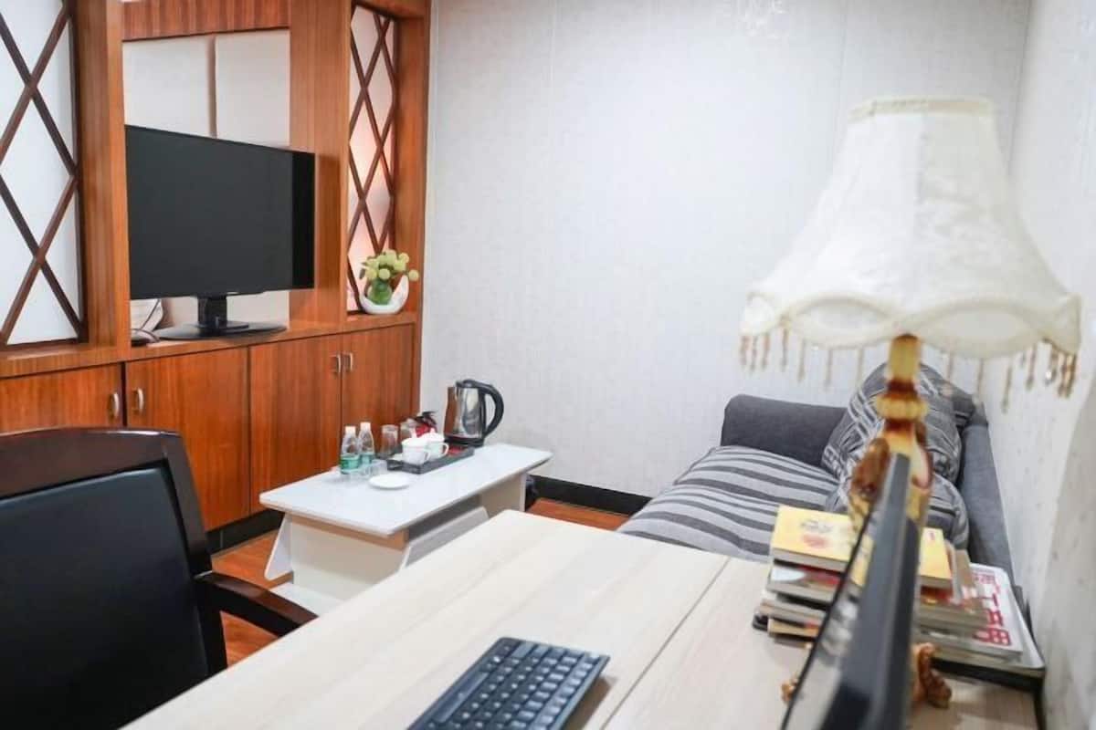 A hotel room with a desk, a television, a sofa, and a lamp.
