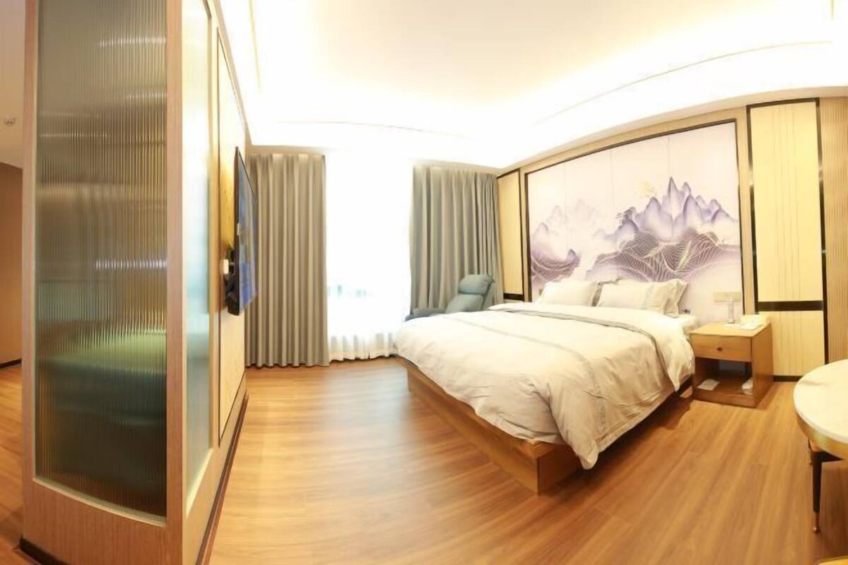 A hotel room with a bed, a chair, a bedside table, and a large window with curtains.