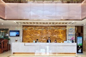 A hotel reception area with a marble counter, a digital screen, and a decorative wall. - Shibazi Hotel (Yangjiang)