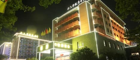 A multi-story hotel with a prominent entrance, multiple balconies, and a well-lit facade.