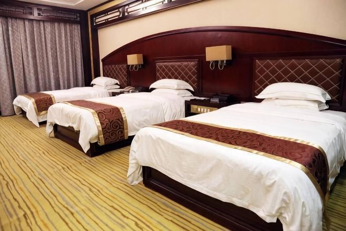 A hotel room with three beds, a wooden headboard, and a carpeted floor.