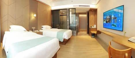 A hotel room with two beds, a desk, a chair, a TV, and a bathroom with a glass door.