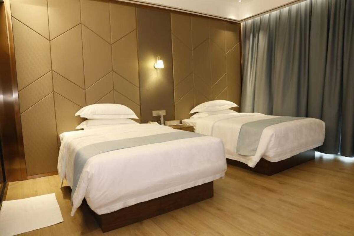 A hotel room with two beds, a wooden floor, a wall with a geometric pattern, and a large window with curtains.