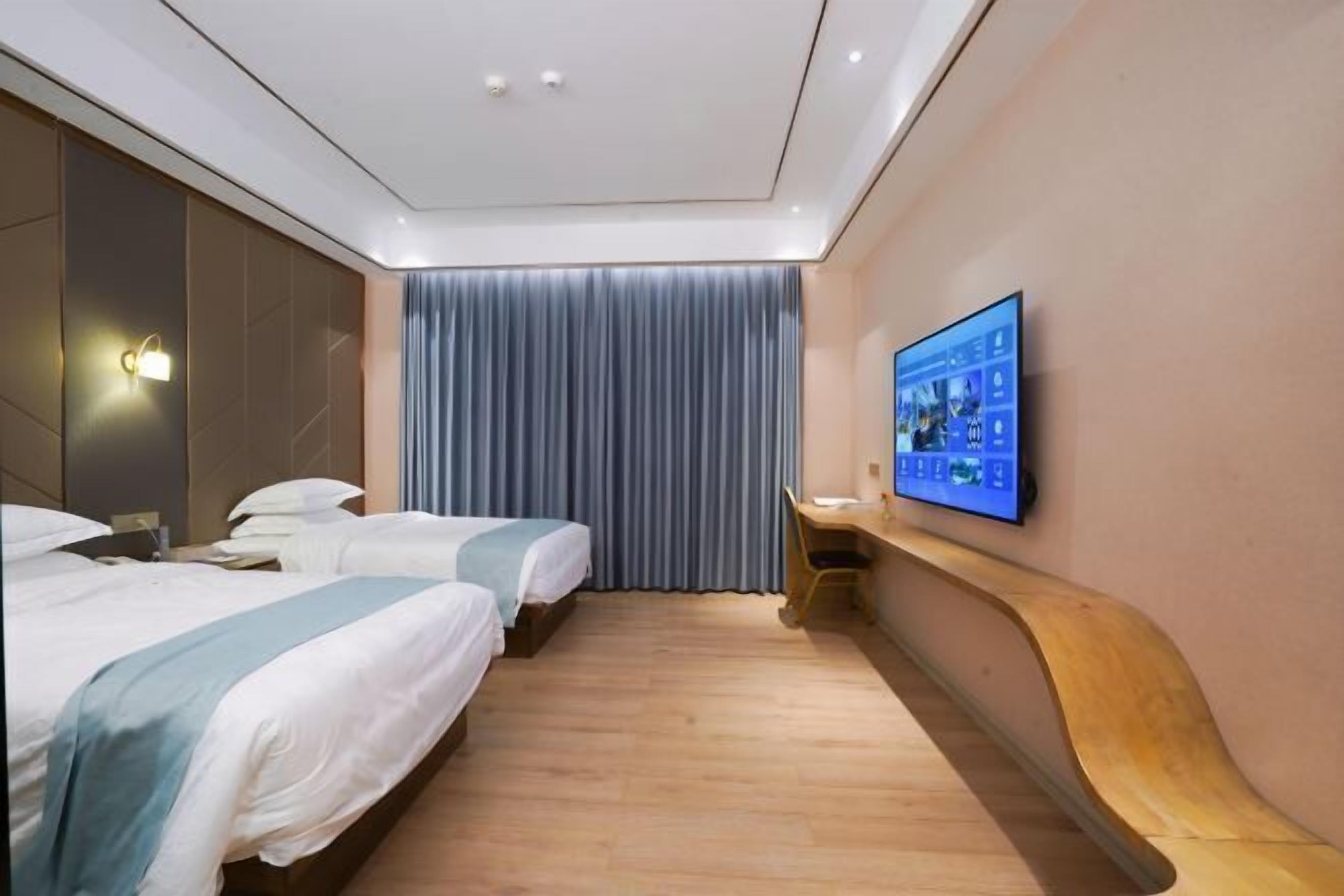 Ett hotellrum med två sängar, ett skrivbord, en TV och ett stort fönster med gardiner.
