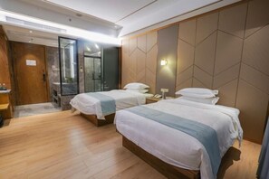 Habitación de hotel con dos camas, suelo de madera, zona de ducha y puerta de madera.