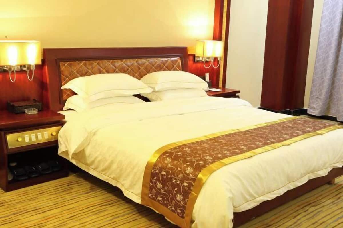 A hotel room with a large bed, two bedside tables, a nightstand, and a lamp.