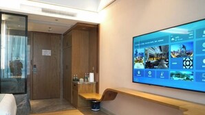 A hotel room with a large wall-mounted TV displaying various images, a wooden bench, a small table with toiletries, and a wooden wardrobe. - Shibazi Hotel (Yangjiang)