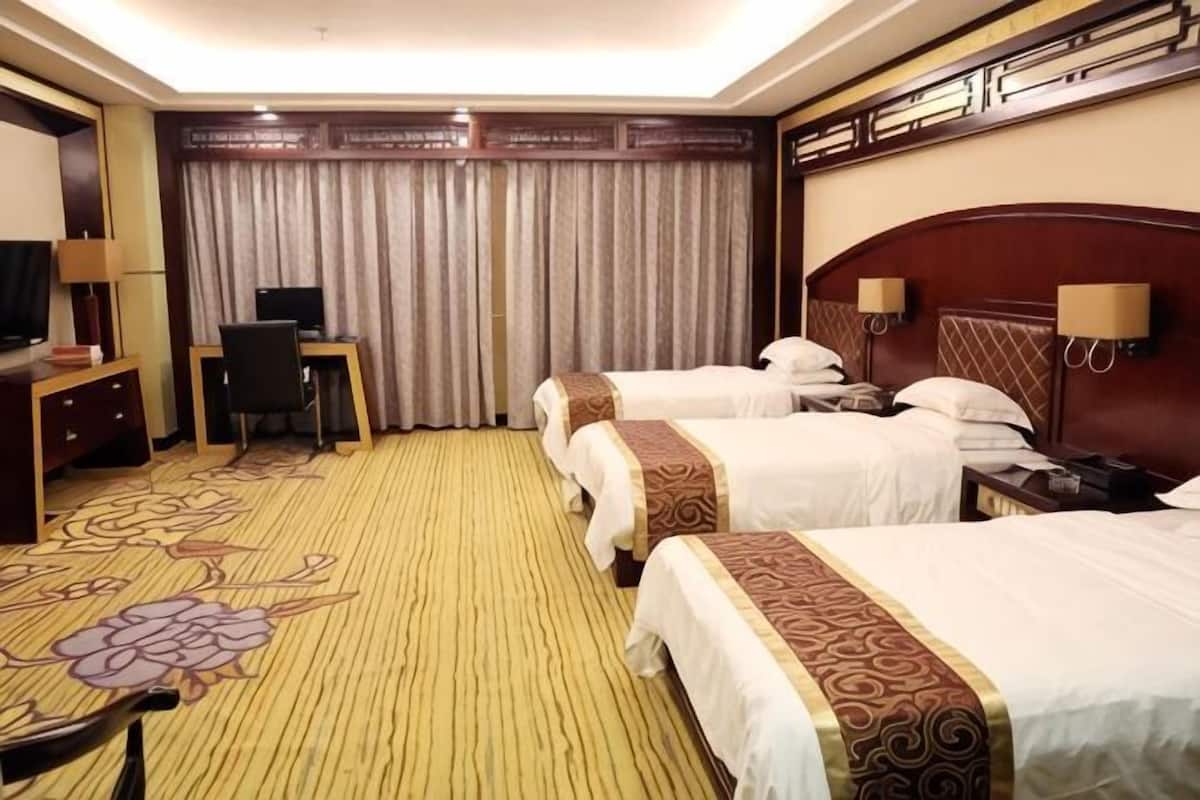 Habitación de hotel con tres camas, un escritorio con silla, un televisor y un ventanal con cortinas.