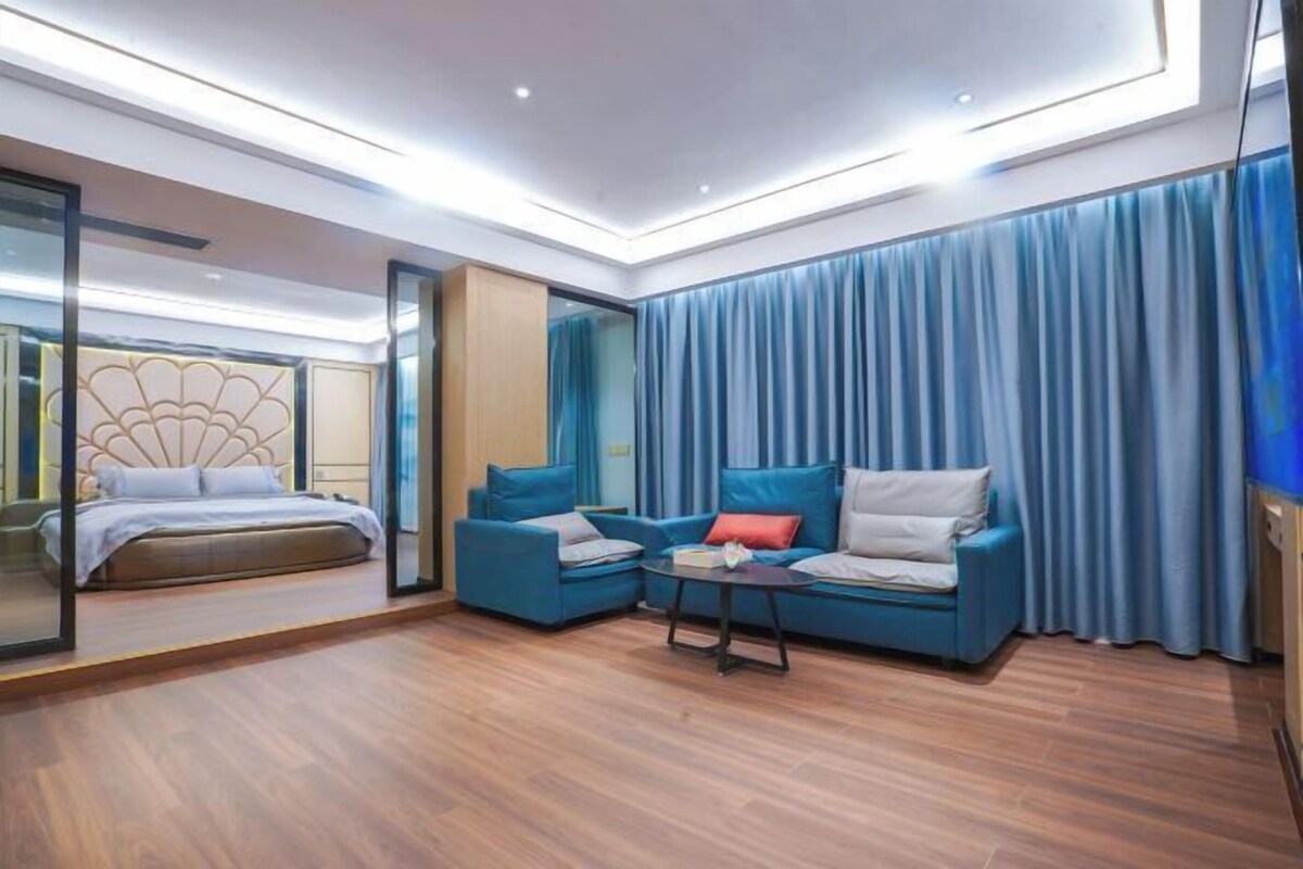 Una habitación de hotel moderna con cama, sofá, mesa de centro y un gran ventanal con cortinas.