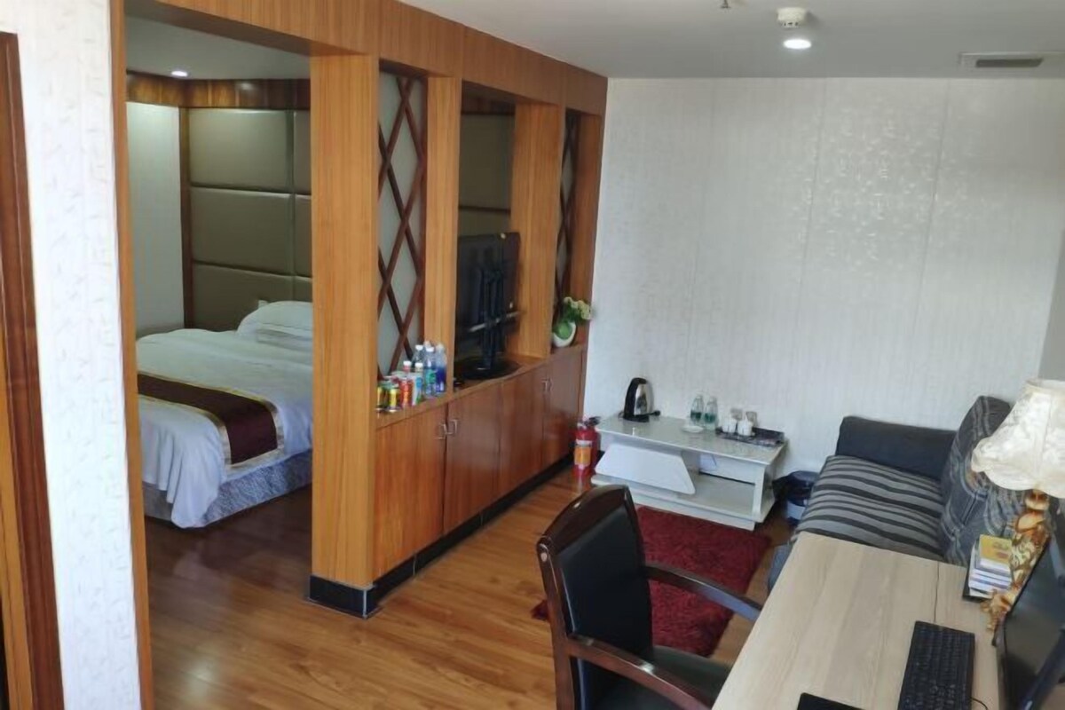 Habitación de hotel compacta con cama, kitchenette pequeña, zona de comedor con mesa y sillas, y sofá.