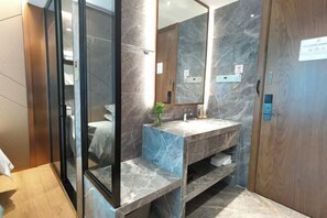 Un baño moderno con tocador de mármol, un espejo grande y una puerta de madera.